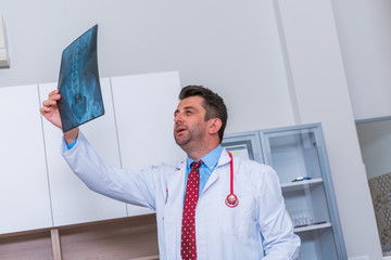 Male Doctor in his mid 40's reading an x-ray image ( radiography ) from a patient hip region ( coxa...