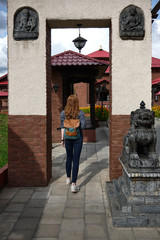 Fototapeta premium Redhead girl in a shirt with a backpack enters the archway into the courtyard with Asian-style buildings, view from back