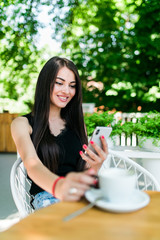 Beautiful young woman sits at a table in a cafe with a cup of coffee and uses the phone