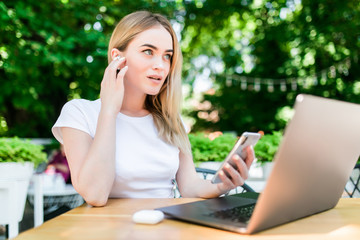 Portrait of pretty woman talking on the phone while sitting in the cafe with laptop and enjoying coffee