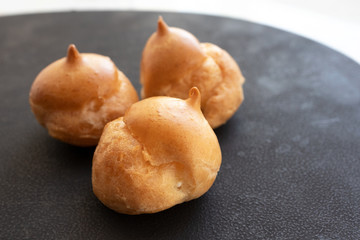 Portion of delicious dessert on black dish with selective focus. Cream puff cakes, close-up. French pastry