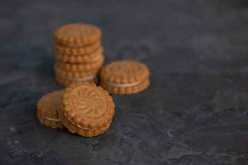 round shortbread cookies with a layer of cream on a dark background. In the background, a blurry stack of cookies. Copy space