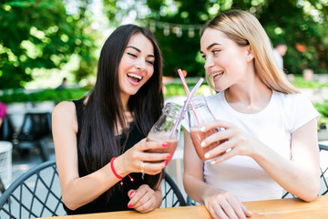 Portrait of cheerful young friends having fresh juice. Two young women at juice bar having a glass of fresh fruit juice together.
