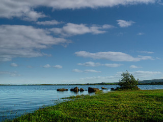 Blue surface of lake Corrib and cloudy sky, Grass covers shore. Warm sunny day.