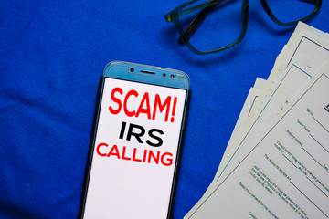 SCAM! IRS Calling text on Smart Phone isolated on office desk. - obrazy, fototapety, plakaty