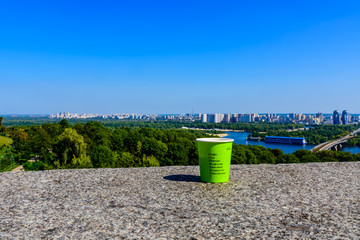 Paper glass of coffee on stone parapet in front of Kiev cityscape. View on residential districts on...