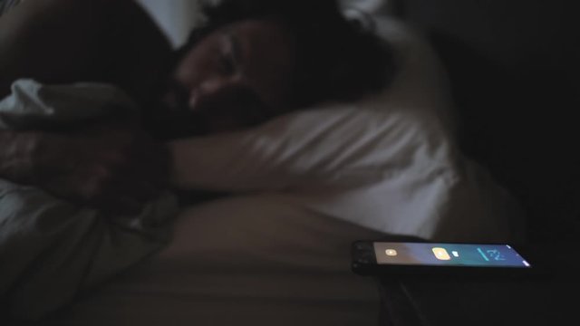 Young man sleeping in a bed woken by a smart phone