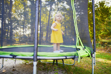 Adorable toddler girl in yellow dress having fun on a trampoline on a summer day