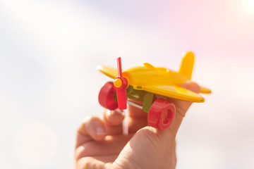 A small toy airplane in a man’s hand against a blue sky with a blurred background. Travel concept