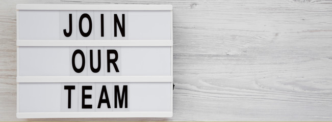 Obraz premium Overhead view, 'Join our team' words on a lightbox on a white wooden background. Top view, from above, flat lay. Space for text.
