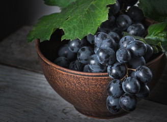 Fresh grapes in a clay plate on a wooden old table.