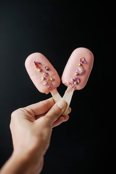 Woman's hand holding two ice-cream Cake pops decorated with sprinkles and rose petals