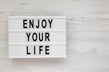 'Enjoy your life' words on a modern board over white wooden background, overhead view. Top view, from above. Flat lay. Copy space.