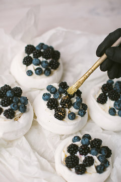 Woman decorating Pavlova desserts with blueberries and blackberries