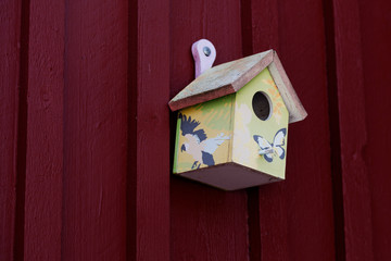 beautifully decorated birdhouse hung on a red wooden wall in Roback