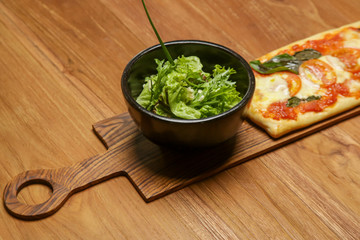 Homemade pizza served with a bowl of green salad on the wooden table