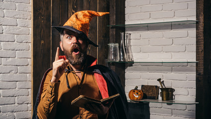 Scary face man with horror Make up holding Pumpkin head jack lantern on sky background. Evil witcher with red hair and beard in a black cloak reading a book of spells. Halloween, holidays celebration.