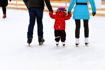 A l boy with dad and mom skates on the rink in the winter. Active family sport, winter holidays,...