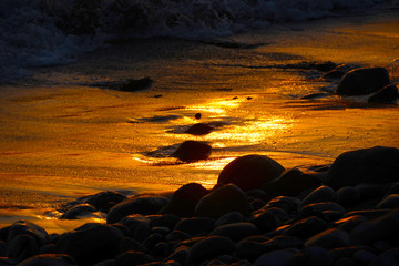 Obraz premium large beach pebbles in waves during sunset as background