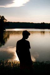 Silhouette of young man at a lake during sunset 