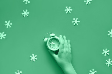 Child's hand holding blue alarm clock showing five to twelve with paper snowflakes toned in neo...
