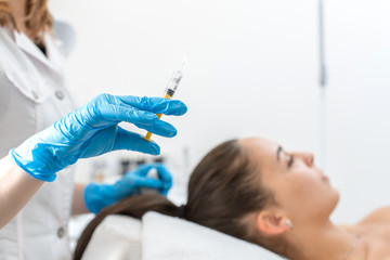 beautician holds a syringe with an rejuvenation injection on the background of the patient. A young...