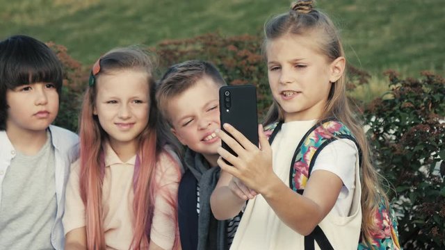 Four children are sitting on a bench and trying to make selfie.
