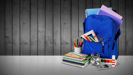 Colorful school supplies in backpack on wooden background