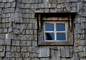 An old window on a grey wall made of weathered shingles