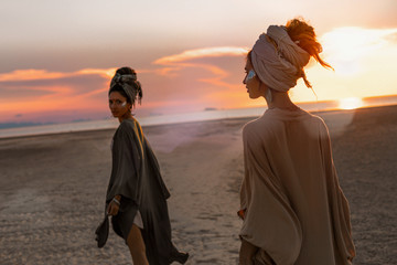 two young beautiful girls in turban walking on the beach at sunset