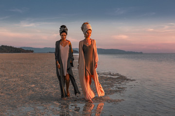 two young beautiful girls in turban walking on the beach at sunset