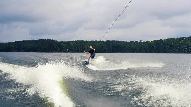 Extreme water sport. Young man doing tricks on wakeboard on lake. Wakeboard rider moving fast in splashes of water