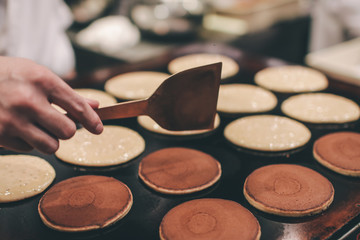 a stall vendor pouring creamy batter on a hot plate to make Dorayaki, a Japanese pancake-like...