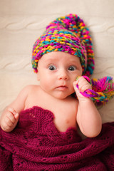 Close portrait of adorable baby in knitted funny gnome hat lies on his back.
