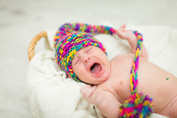 Close portrait of adorable crying baby in knitted funny gnome hat lies on his back in basket