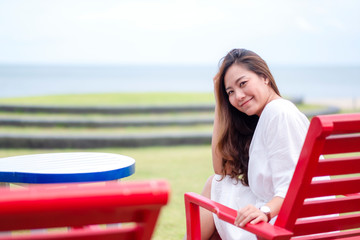 Fototapeta na wymiar A beautiful asian woman enjoy sitting and relaxing on the bench by the sea