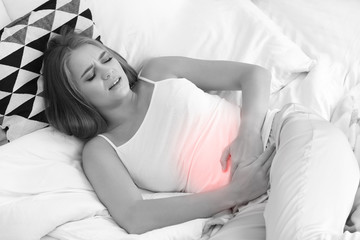 Young woman suffering from abdominal pain in bed