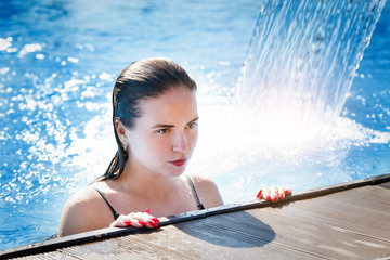 Young beautiful woman under a waterfall in a pool with clear blue water.
