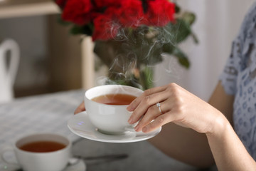 Young woman with engagement ring on her finger drinking tea, closeup