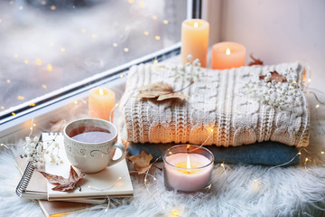 Beautiful autumn composition with burning candles and cup of tea on window sill