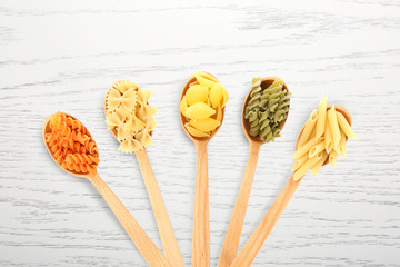 Spoons with assortment of uncooked pasta on white background