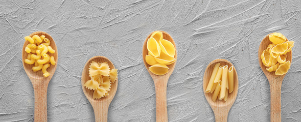 Wooden spoons with different uncooked pasta on grey table