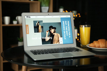 Laptop with open page of fashion blog on table