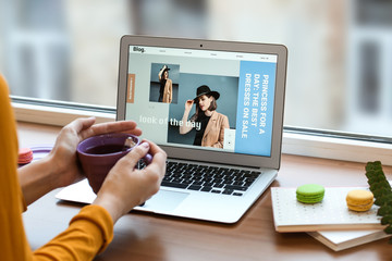 Female fashion blogger working on laptop and drinking coffee near window