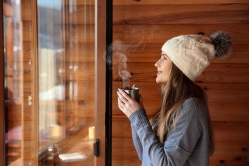 Woman drinking hot mulled wine near window in morning