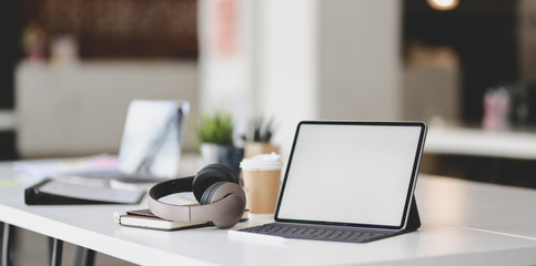 Blank screen tablet with on-ear headphones and office supplies on white table