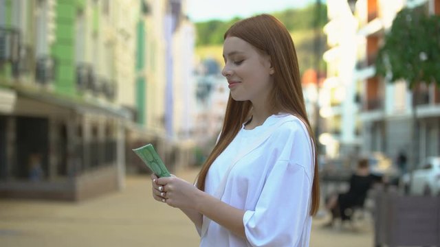 Excited teenage girl holding euro banknotes standing on street, first salary