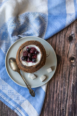 Berry dessert with yogurt in a cup of coconut on a wooden background. Blackberries, raspberries, blueberries, black currants. Blue napkin