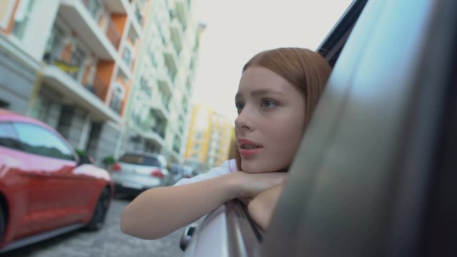 Sad girl saying good bye to native city sitting on back seat of car, relocation