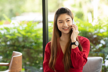 Business Asian woman wearing red dress working with laptop smile and talking with customer in smartphone get idea and requirement for success job outside office in coffee shop,Small Business Concept